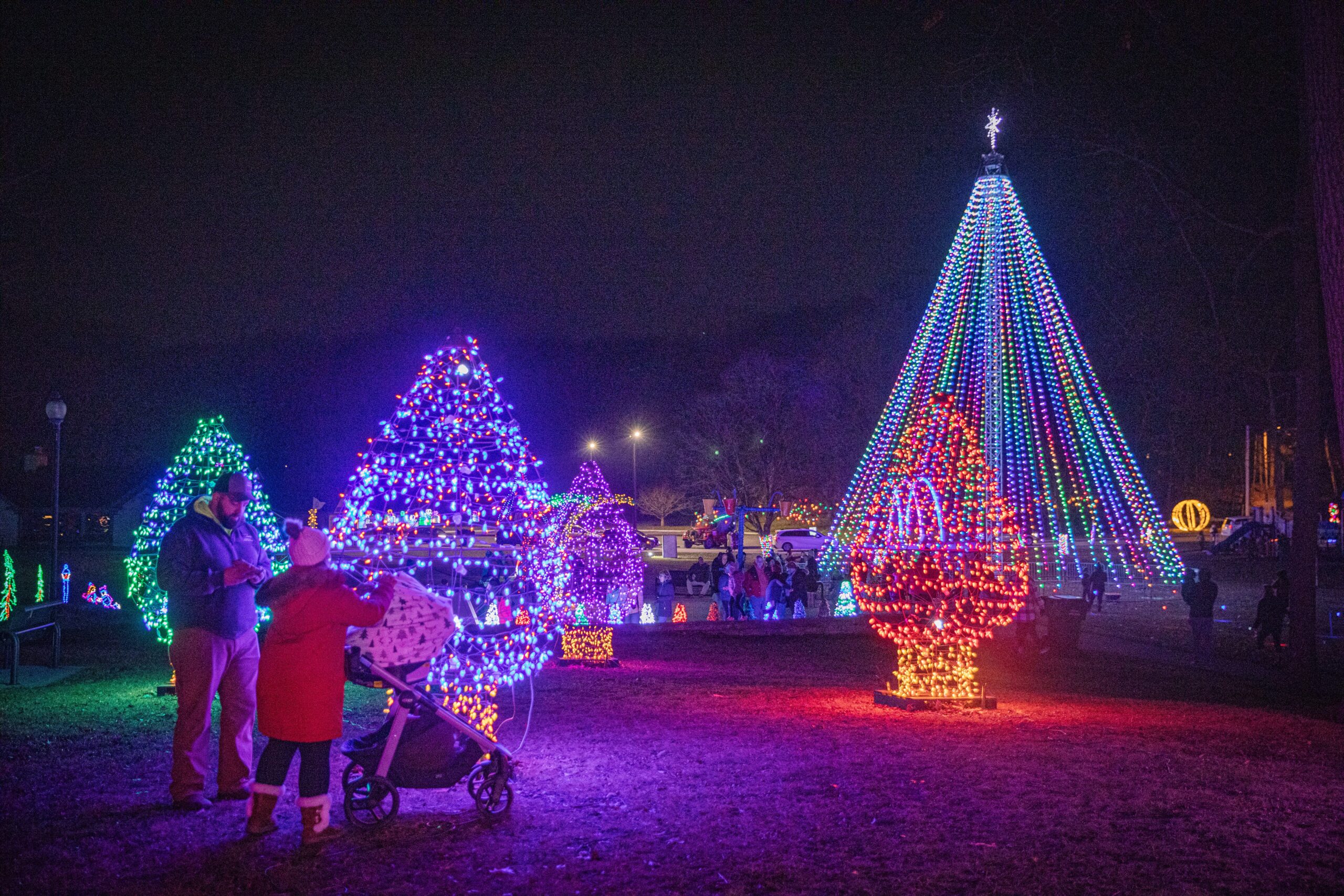 Man and woman with baby stroller next to trees with holiday lights